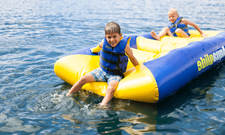 Two young boys sitting on a float in the lake with life vests on