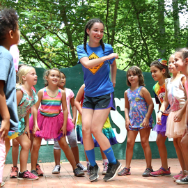 Counselor dancing in the middle of a circle of young girl campers