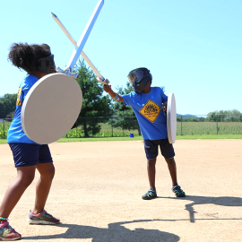 Campers wearing LARPing gear role playing a sword fight