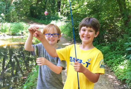 Two boys holding up a small fish hanging from their fishing rod