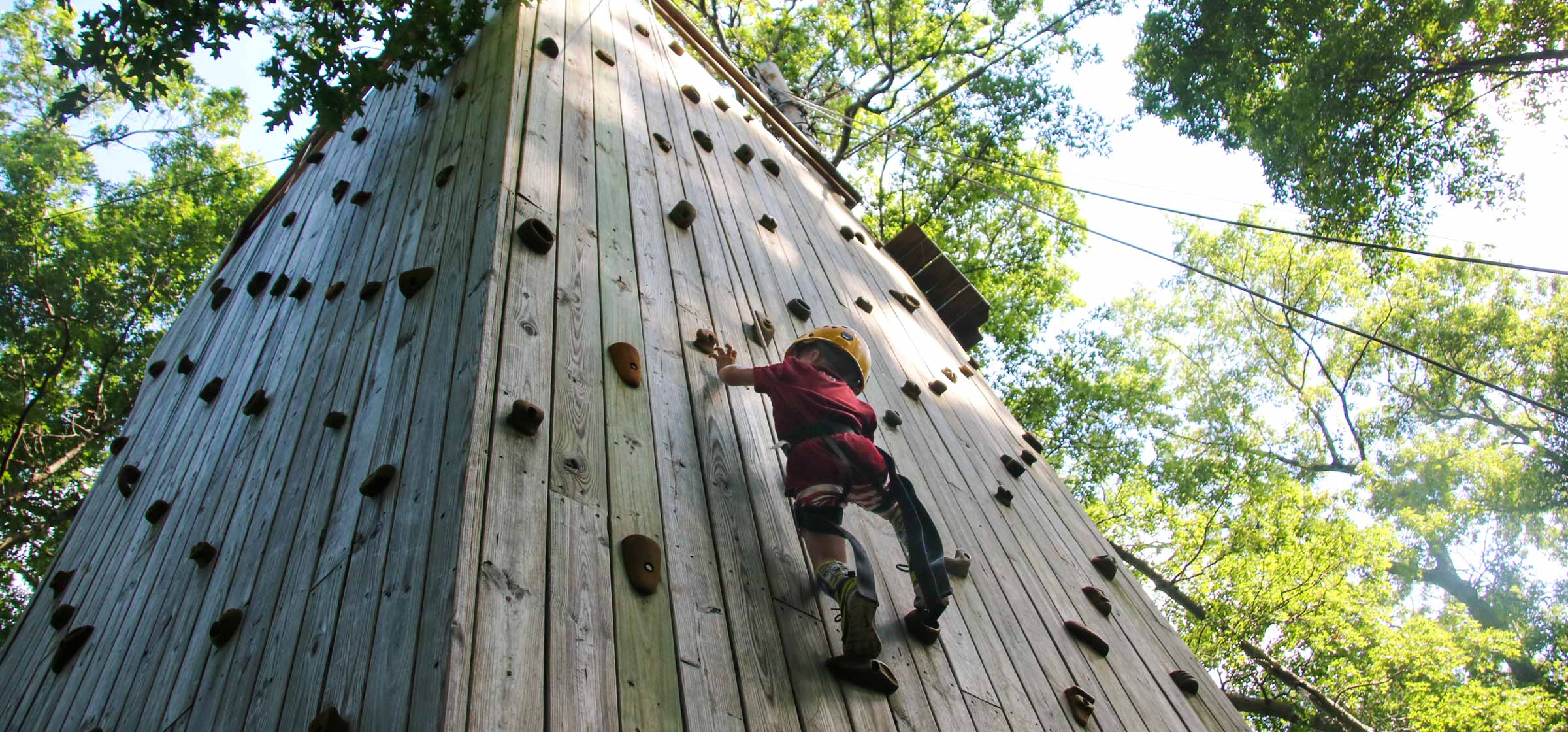 Camper climbing an advanced climbing wall outside