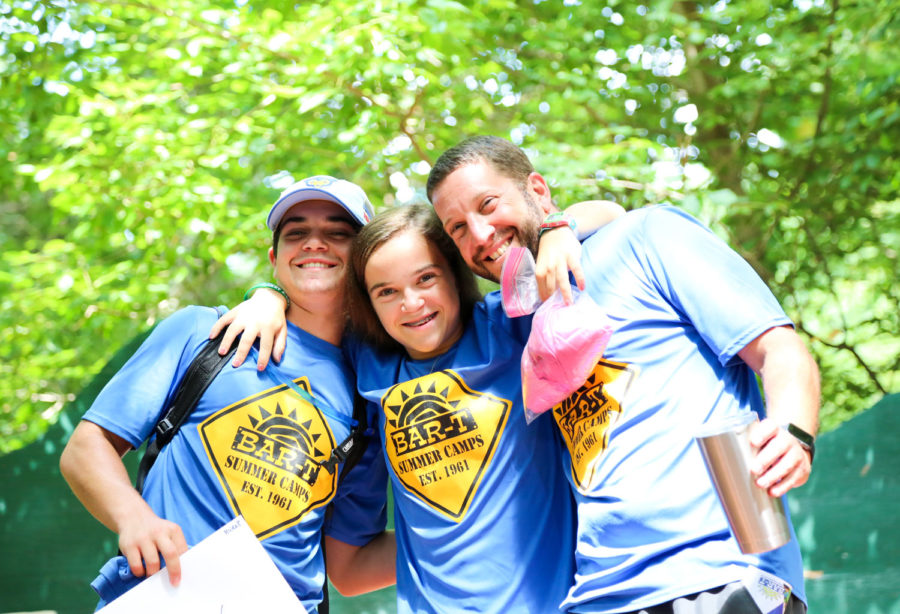 A camper in the middle of two counselors with her arms around them, all three smiling