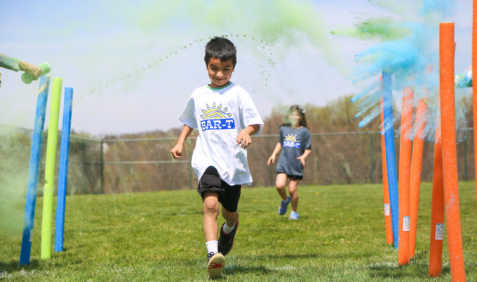 Camper running in a color run with color chalk being thrown at him