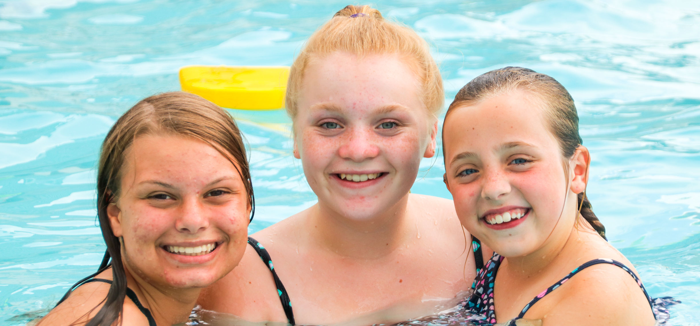 Three campers in the swimming pool smiling for a photo