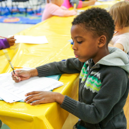 Boy camper working on homework at a long table next to other kids