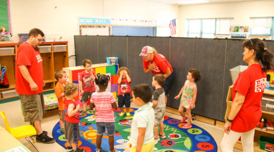 Campers in a classroom standing in a circle playing a game with a teacher