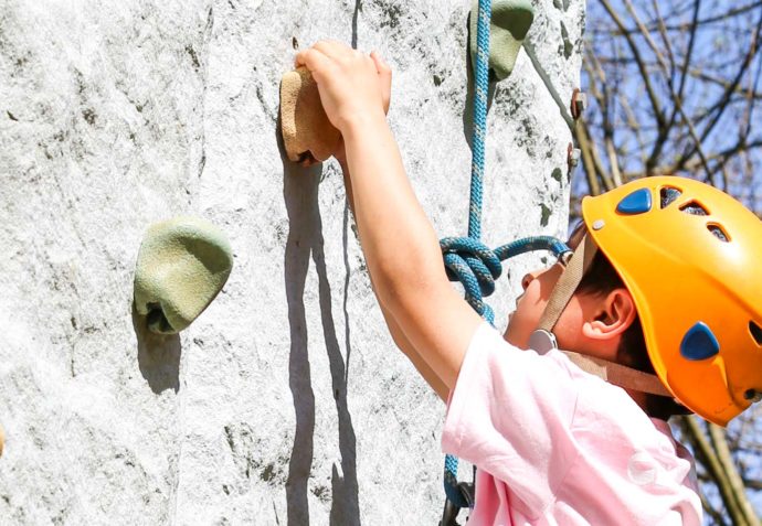 Boy with a helmet climbing a rock wall outside in a harness