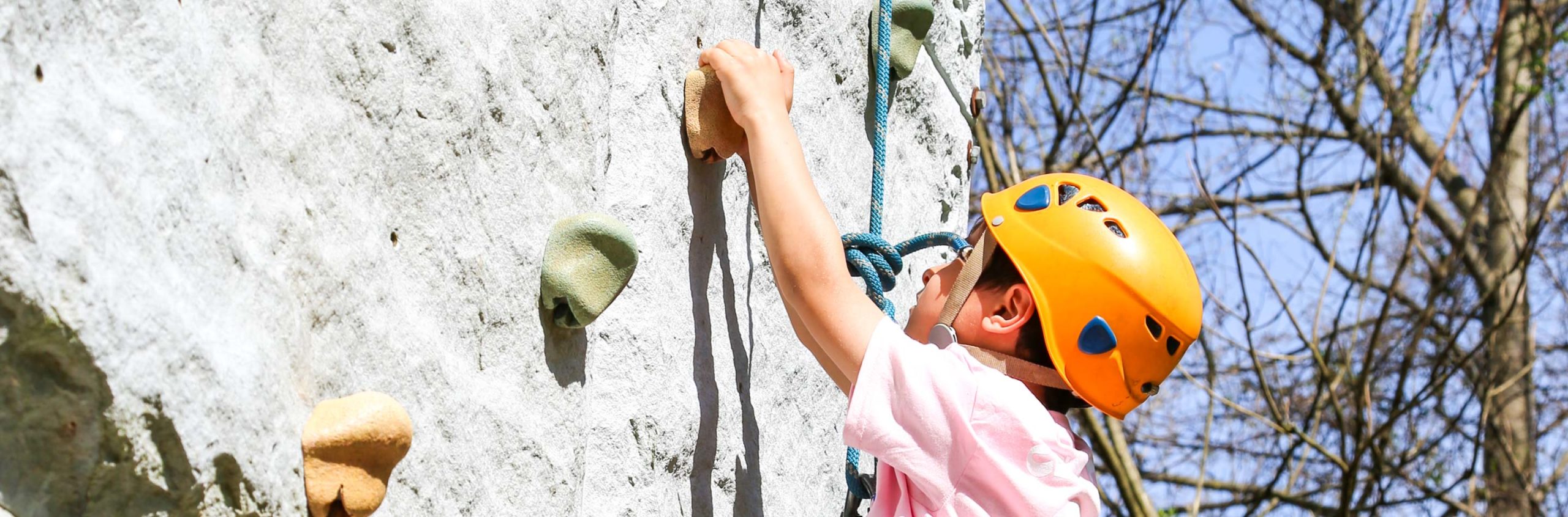 Boy with a helmet climbing a rock wall outside in a harness