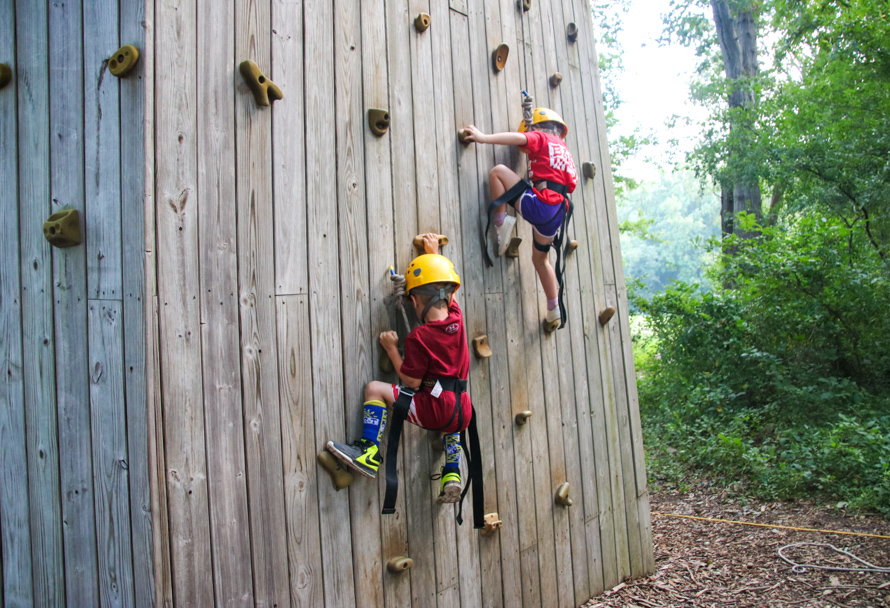 Two campers climbing up a rock wall outside