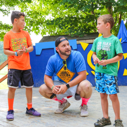 Counselor crouching down talking to two campers on the stage