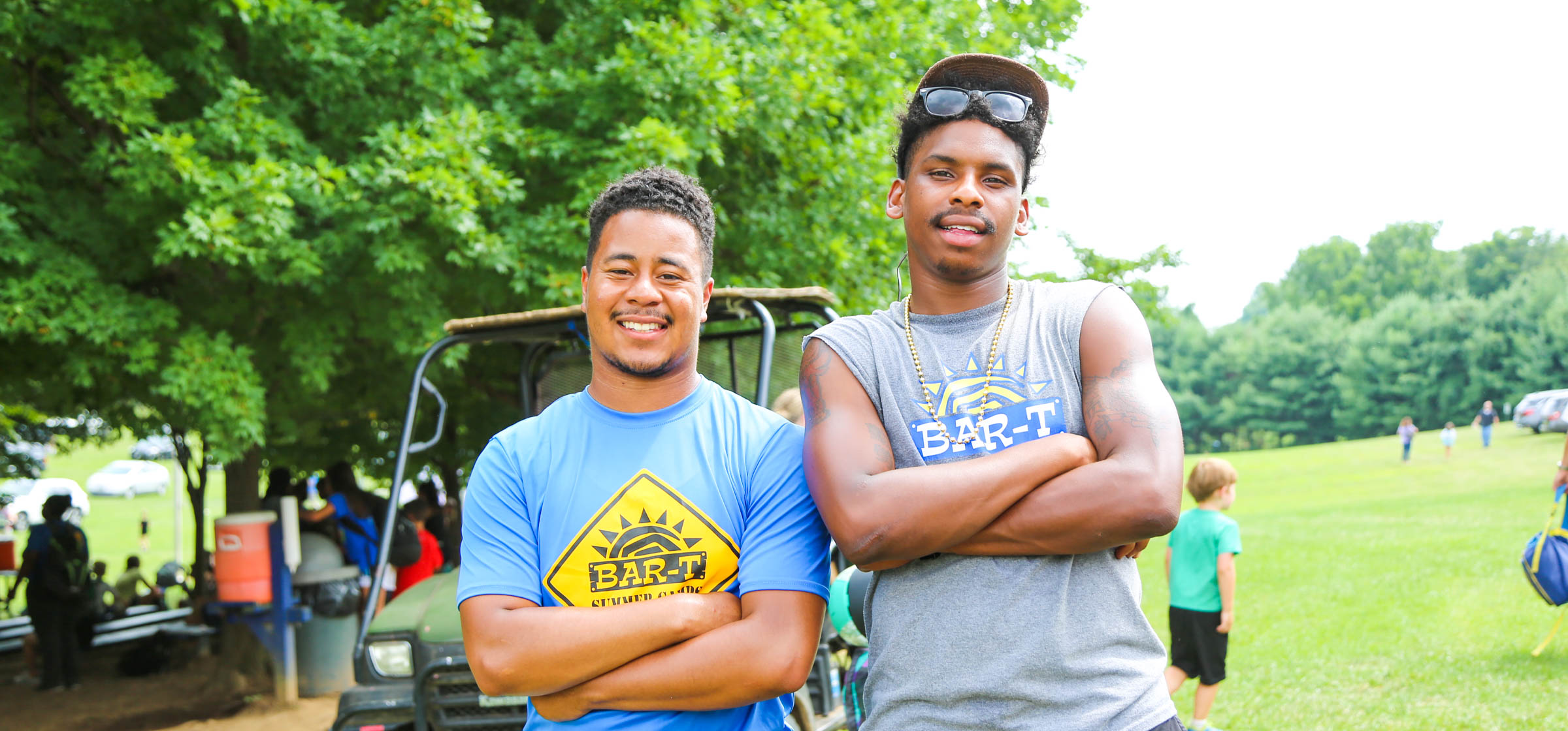 Two male counselors standing with their arms crossed smiling for the photo by a golf cart outside