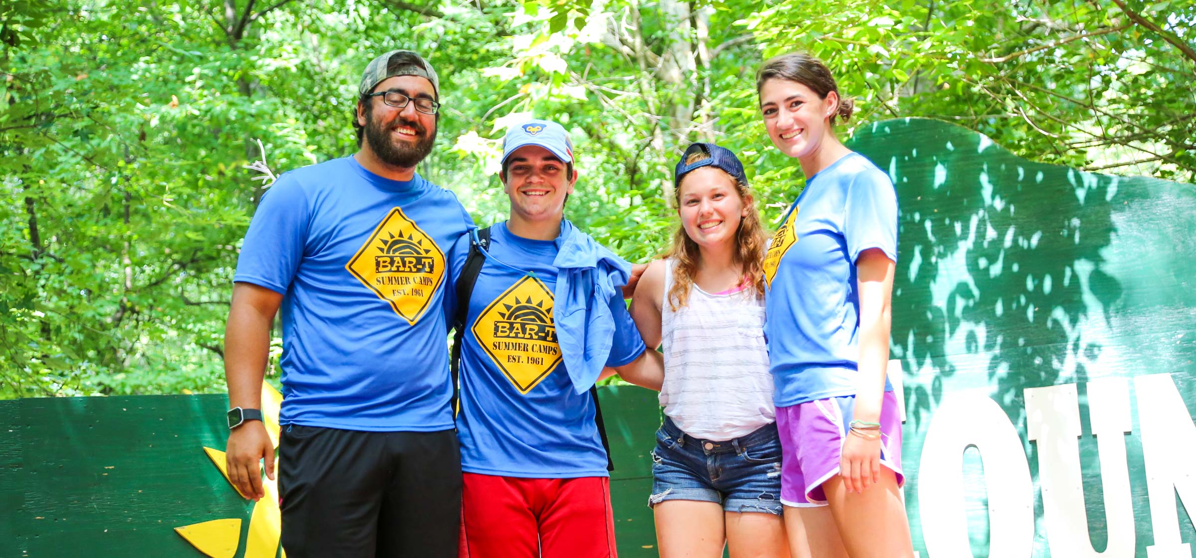 Four counselors standing together for a photo outside on a small stage surrounded by trees