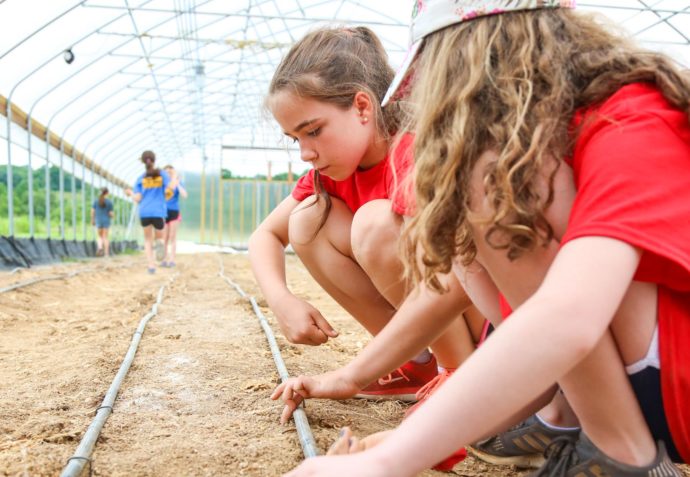 Two campers crouching on the ground feeling the soil of the green house