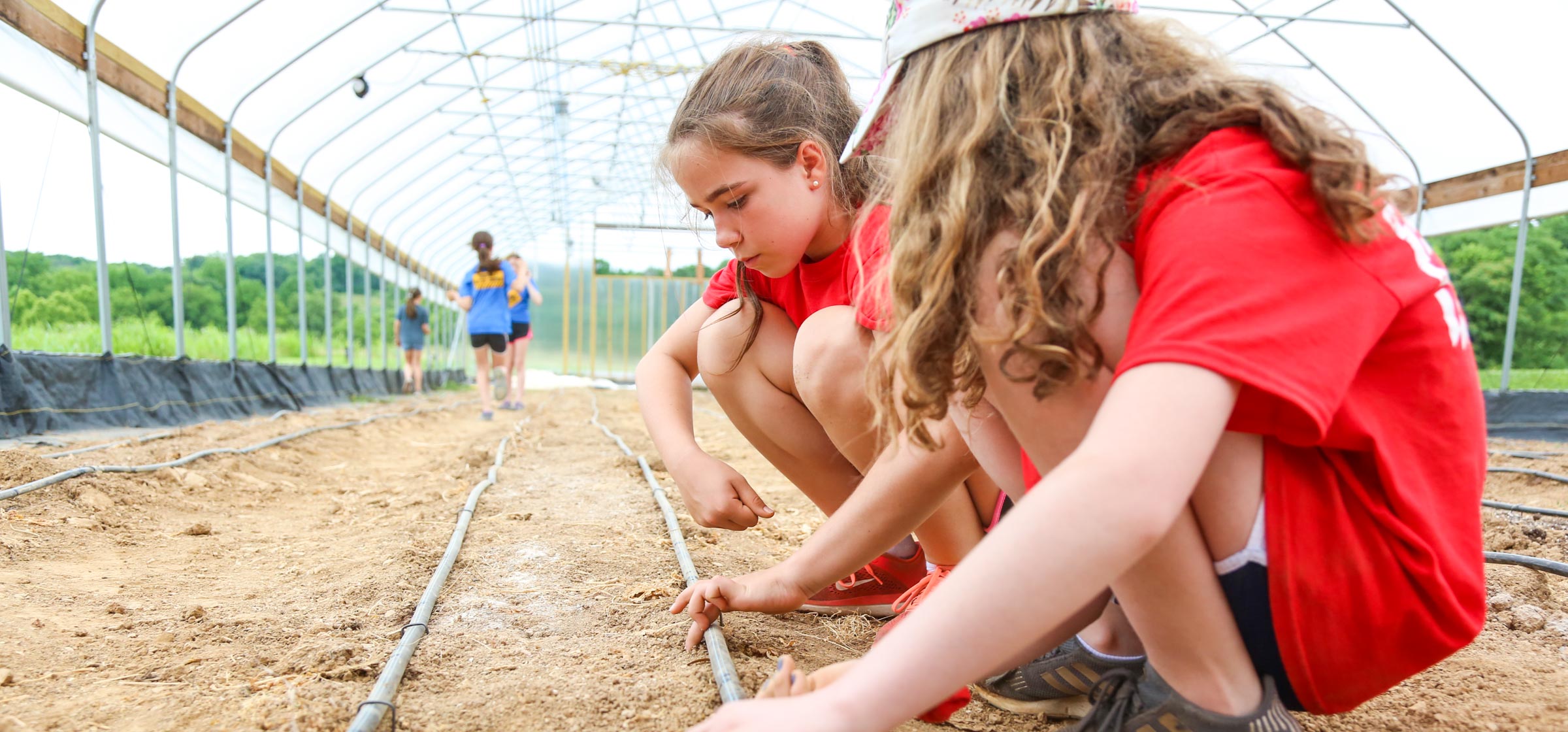 Two campers crouching on the ground feeling the soil of the green house