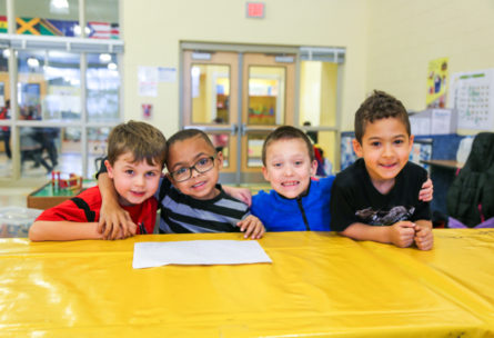 Four boys sitting at a table with arms around each other smiling for the photo