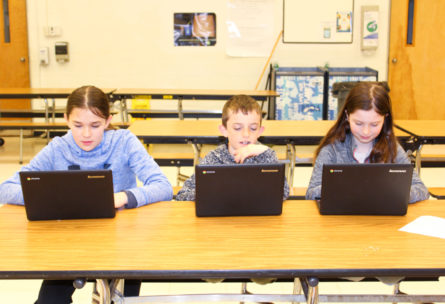 Three students working on laptops at a table