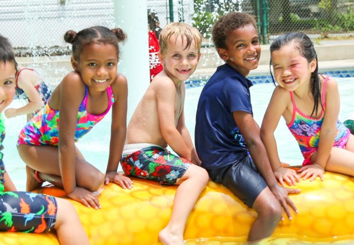 Five friends at a water park sitting on an inflatable toy in a shallow pool