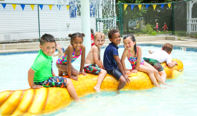 Five friends at a water park sitting on an inflatable toy in a shallow pool