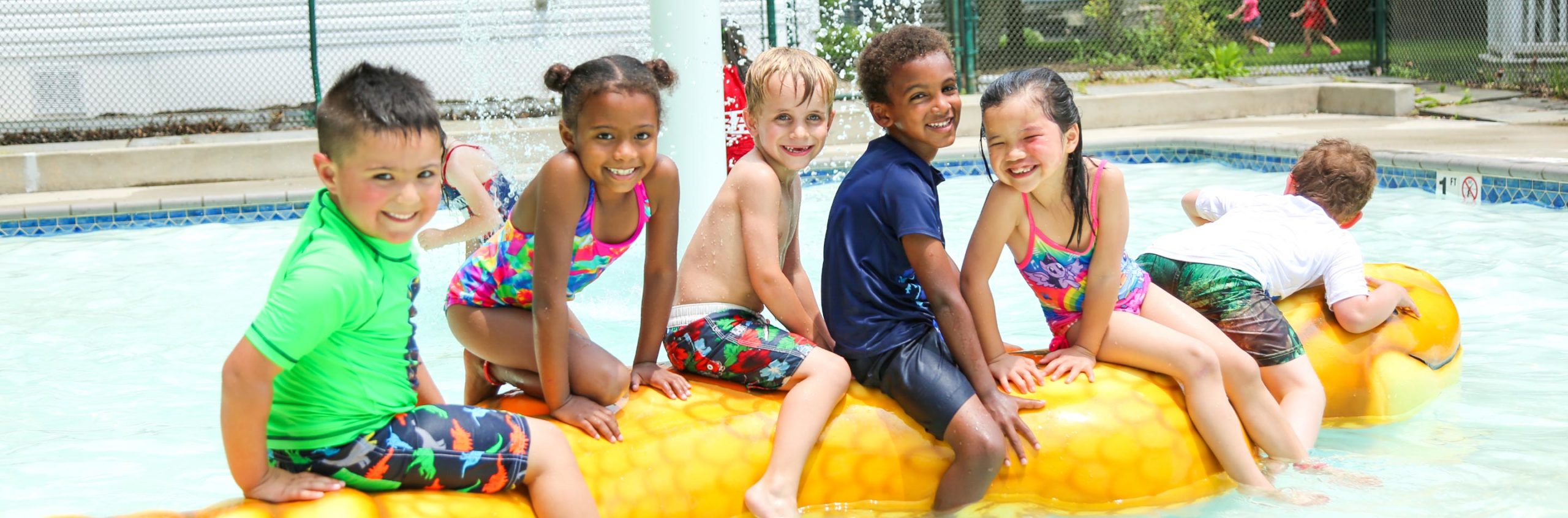Five friends at a water park sitting on an inflatable toy in a shallow pool
