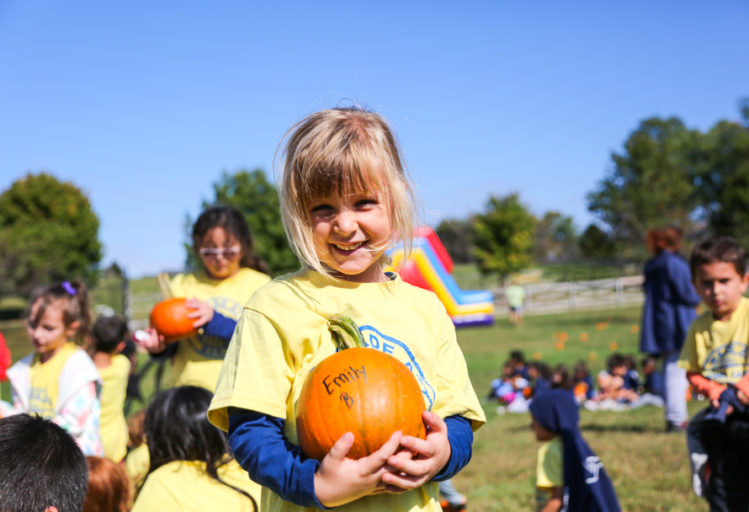 Young girl camper holding a small pumpkin and smiling