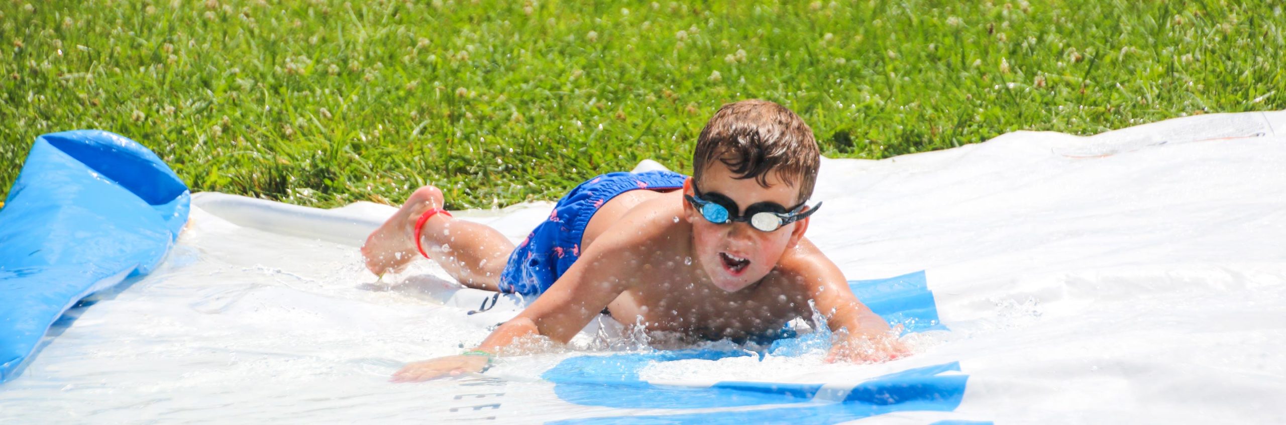 Boy with goggles sliding down a slip n slide on his tummy