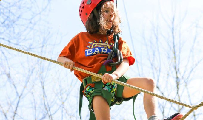 Camper in helmet and straps walking on a high ropes course