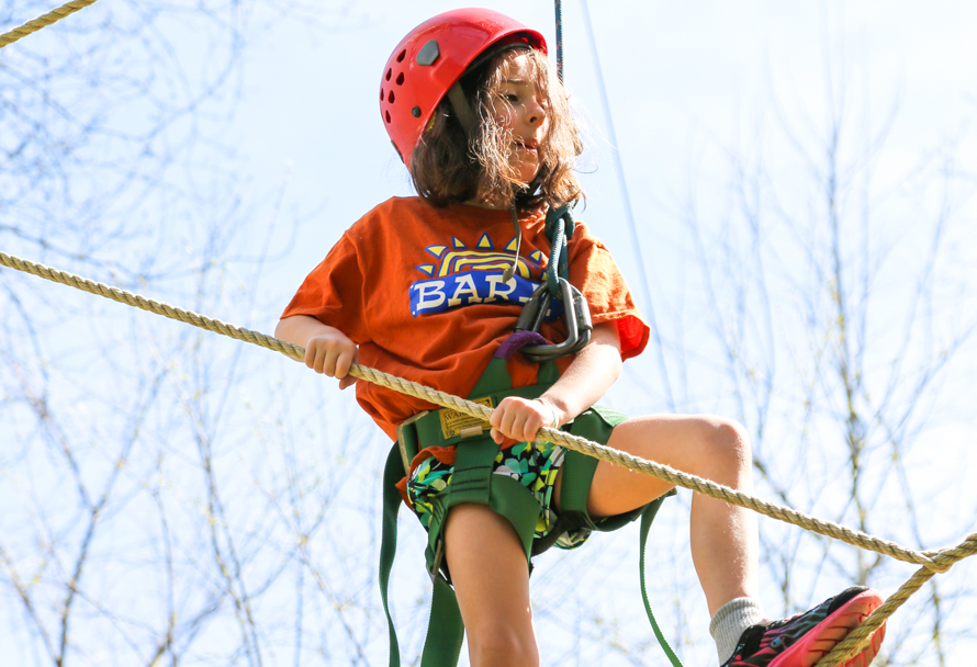 Camper in helmet and straps walking on a high ropes course