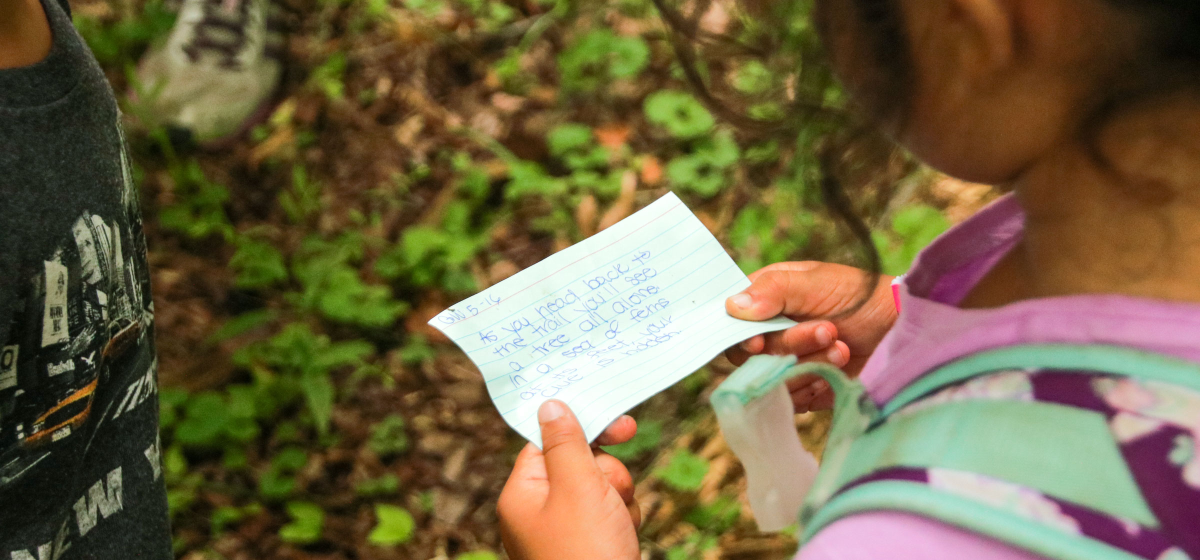 Young girl camper holding a notecard with a scavenger hunt clue