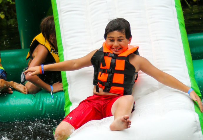 Camper sliding down a large inflatable slide into the lake