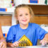 Young girl camper sitting at a table working on an art project smiling at the camera