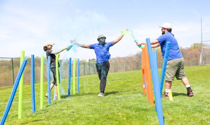 Counselor running through the color run course getting sprayed with color by other counselors