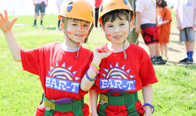 Two campers with helmets on ready to climb the rock wall