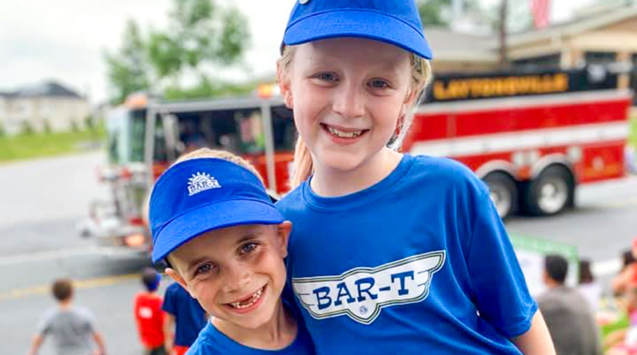 Dagny & Frankie with blue shirts and hats on smiling together for a photo