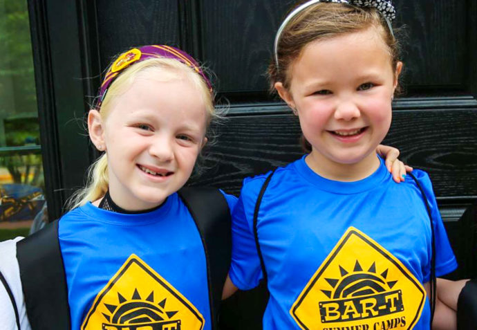 Four young friends with arms around each other smiling for a photo with backpacks on