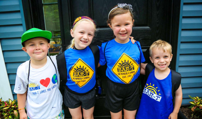 Four young friends with arms around each other smiling for a photo with backpacks on