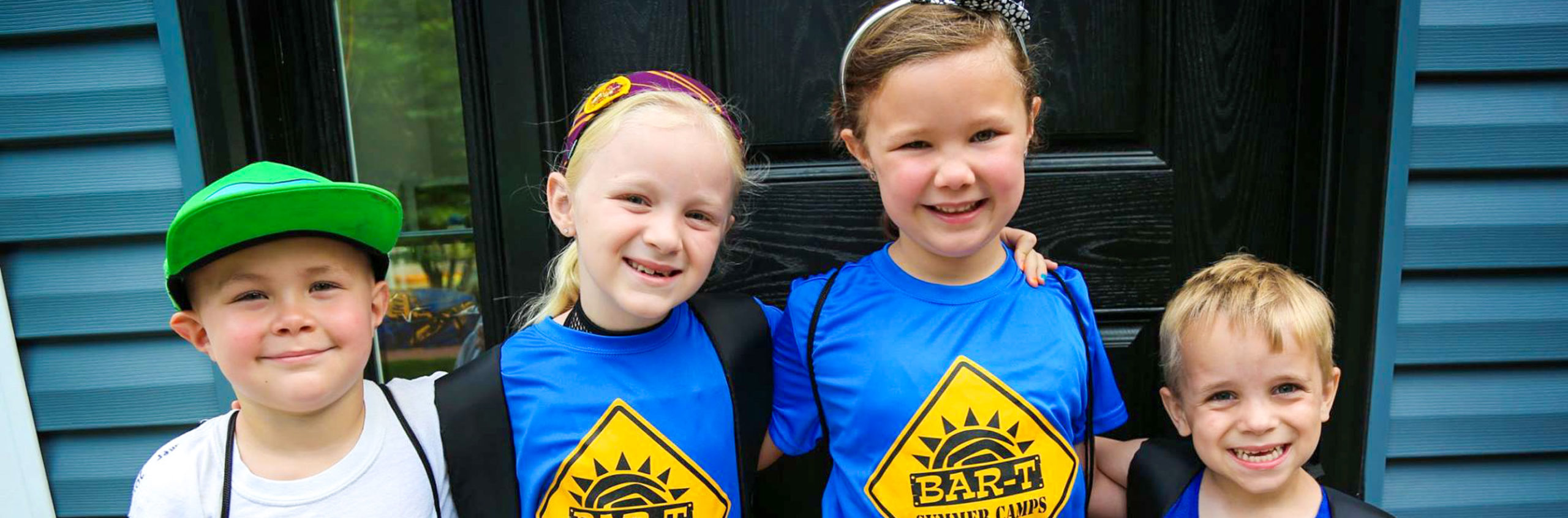 Four young friends with arms around each other smiling for a photo with backpacks on