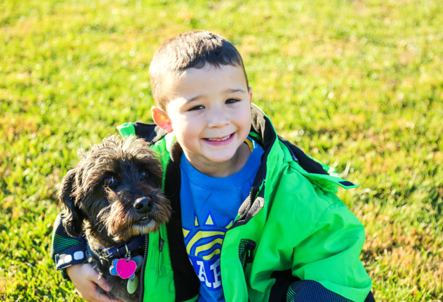 Young boy sitting and smiling next to a small black dog