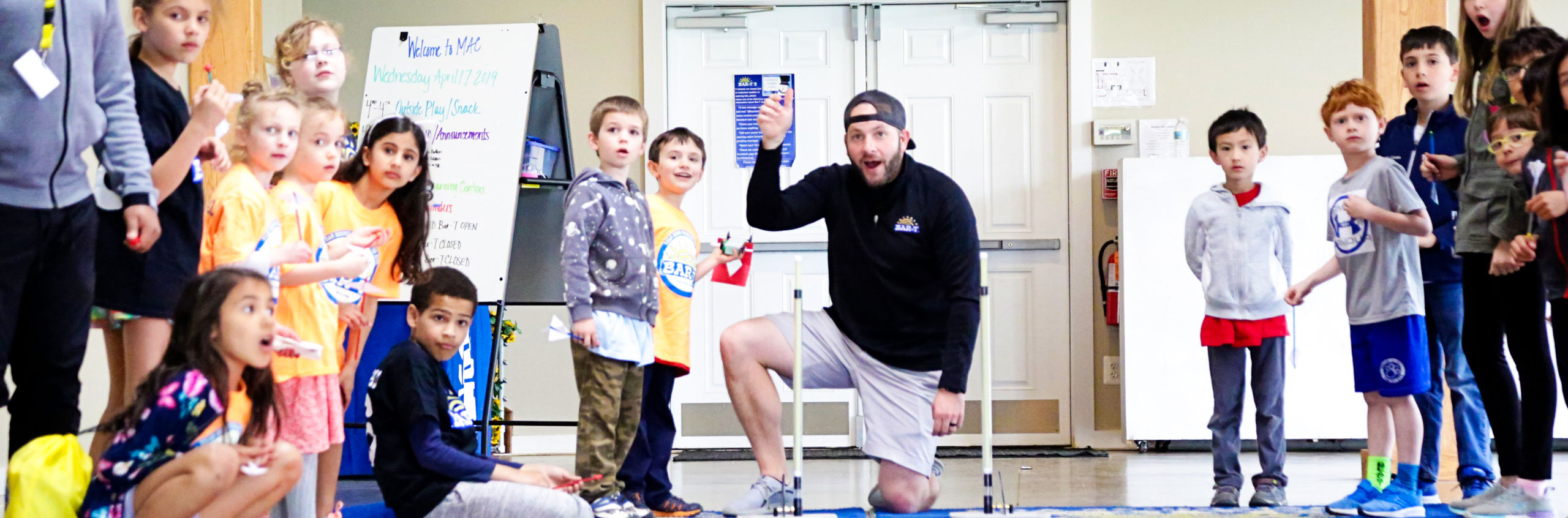 Group of kids watching staff members show them how to play a game inside