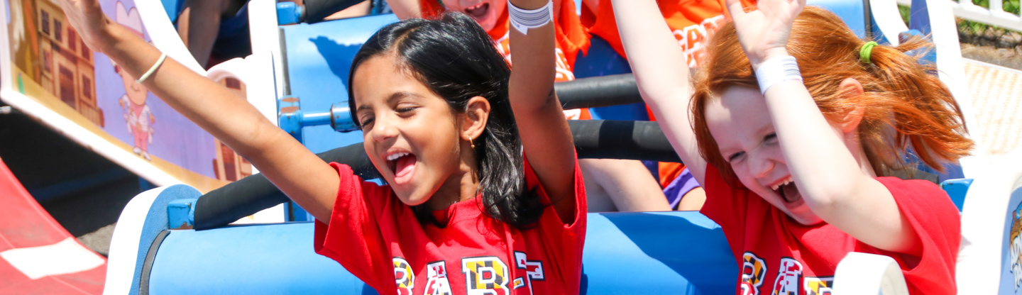 Two girls riding a fair ride with their hands up and smiling